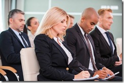 People at the conference. Group of business people in formalwear sitting at the chairs in conference hall and writing something gin their note pads 